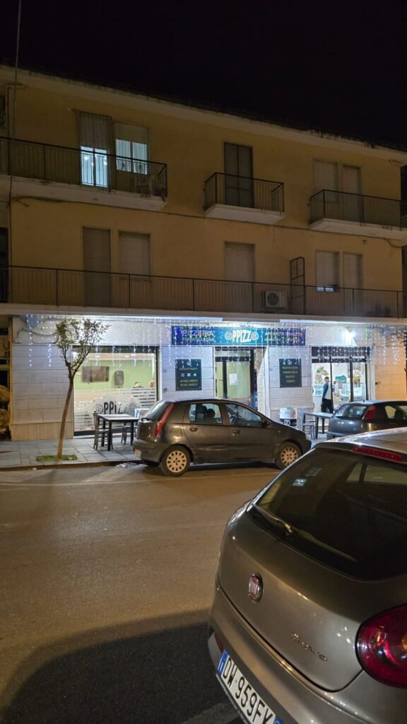Fachada iluminada de la pizzería @PPIZZ@ en Lamezia Terme, vista nocturna.