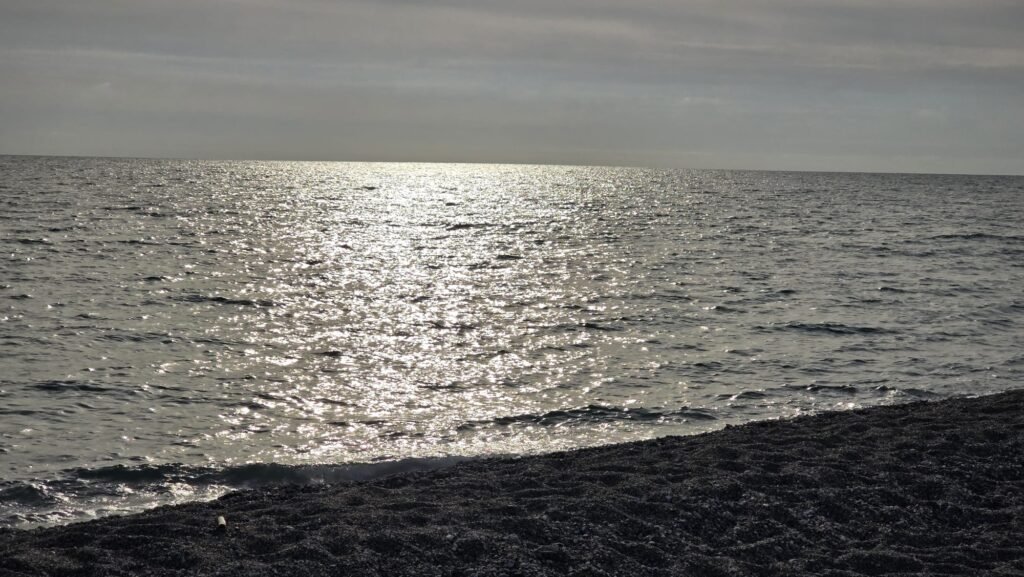 Playa de Lamezia Terme al atardecer, con cielo dorado y olas suaves.