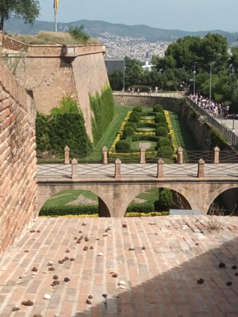 Vista lateral del Castell de Montjuïc con jardines de estilo colonial y vegetación cuidada en Barcelona
